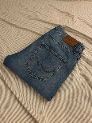 Tapered/Mike jeans från Jack & Jones - Klassiska blå jeans i rak modell med fem fickor och snygg läderpatch bak i midjan. Jeansen har kontrastsömmar och är tillverkade i slitstarkt denimtyg. Perfekta för en avslappnad och trendig look.