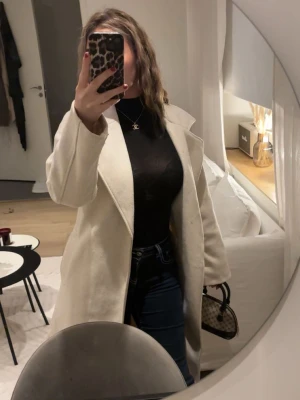 Stilren vit kappa  - Säljer en snygg vit kappa. Kappan har en minimalistisk design och är perfekt för dig som gillar en clean look. Passar till både jeans och klänning. Materialet ser ut att vara ullblandning.