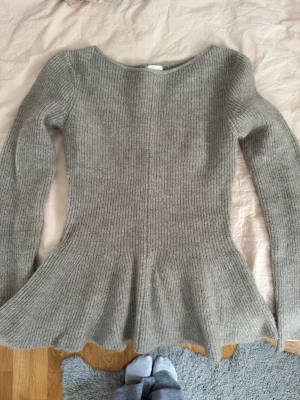 Beige ribbstickad peplumtröja - Säljer en beige ribbstickad tröja med peplumskärning och långa ärmar. Tröjan har rund halsringning och är figurnära upptill med utsvängd nederdel. Perfekt för dig som gillar en feminin och trendig look.