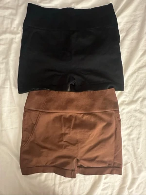 Två par höga shorts i svart och brunt - Två par shorts i olika färger, ett par i svart och ett par i brunt. Båda har hög midja och är tillverkade i ett stretchigt material som passar perfekt till träning eller avslappnade dagar. 