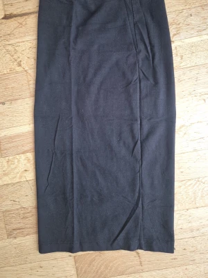 Svart långkjol från Divided XS - En svart långkjol från Divided i storlek XS. Kjolen har en rak och enkel design utan synliga detaljer eller mönster, vilket gör den lätt att matcha med olika stilar. Tillverkad i ett mjukt och stretchigt material som känns bekvämt. Välanvänd. 