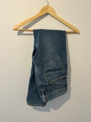 Blå jeans från Nudie Jeans lean dean - Säljer ett par klassiska blå jeans från Nudie Jeans Co i storlek 30/30. Jeansen har raka ben, fem fickor och tydliga kontrastsömmar. Tillverkade i slitstarkt denimtyg som ger en tidlös look. Perfekta för dig som gillar en enkel och clean stil.