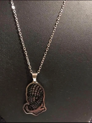 Palestina keffya Silverfärgat halsband med bönande händer - Snyggt halsband i silverfärg med en unik berlock som föreställer bönande händer med detaljerat mönster. Kedjan är tunn och stilren, vilket gör att berlocken står i fokus. Perfekt accessoar för dig som gillar statement-smycken.