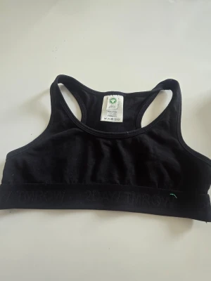 Svart sport-bh från Lindex - En svart sport-bh från Lindex i storlek 134/140. Bh:n har bred resår med diskret text, brottarrygg och är tillverkad i mjukt, stretchigt material. Perfekt för träning eller vardag.