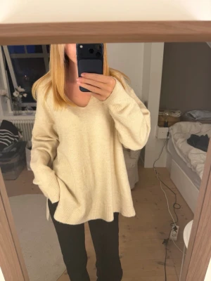 Oversized beige stickad tröja - Mysig oversized stickad tröja i beige med v-ringning och långa ärmar. Tröjan har en avslappnad passform och ribbstickade muddar vid ärmslut och nederkant. Perfekt för lager-på-lager och chill dagar.