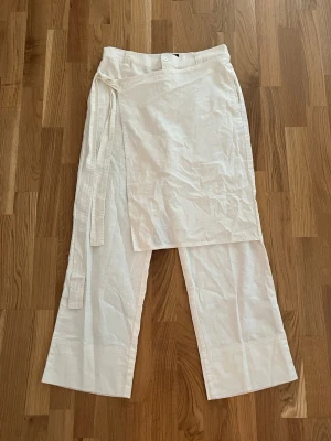 Layered wrap linnebyxor  - Säljer ett par vita linnebyxor från ASOS DESIGN i storlek EU 38. Byxorna har en unik omlott-detalj framtill med knytband i midjan och raka, vida ben. Tillverkade i ett luftigt linnematerial som passar perfekt till sommaren.