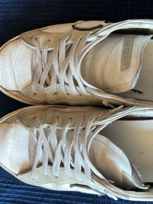 Vita Philippe Model sneakers - Snygga vita sneakers från Philippe Model med klassisk låg profil och svarta detaljer på hälen. Skorna har vita skosnören, diskret logga på sidan och är tillverkade i läder för en stilren look. Originalbox och påse medkommer ej, Skicket är lagom bra, köptes i höstas och användes under vintern då sulorna tog lite skada på grund av blöthet och slets upp lite inuti, annars ser man resten på bilderna. Ny pris: 3600 mitt pris: 2000. Priset är inte hugget i sten