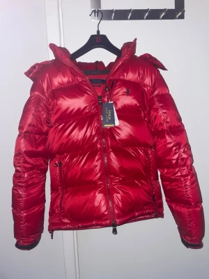 Röd pufferjacka med huva - Snygg röd dunjacka från Ralph Lauren. Storlek S, skulle säga att dessa jackor dock är stora i storleken. Jag köpte denna från Zalando förra året så har använt den en vinter, så den är väldigt fräsch. 