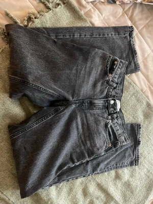 Svarta raka jeans med hög midja - Säljer ett par svarta jeans med rak passform och hög midja. Jeansen har klassiska fem fickor och bälteshällor. Materialet är kraftig denim i bomull och färgen är tvättad svart för en vintagekänsla. Perfekta till en avslappnad streetwear-look.