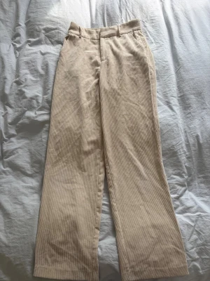 Beiga raka manchesterbyxor - Säljer ett par beiga manchesterbyxor med raka ben och hög midja. Byxorna har bälteshällor och sidofickor, perfekta för en chill och stilren look. Materialet är mjukt och ger en skön vintagekänsla.