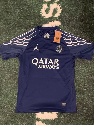 Blå PSG x Jordan matchtröja🧵 - Snygg blå matchtröja från PSG x Jordan med vita detaljer och loggor. Tröjan har korta ärmar, rund hals och ett unikt mönster på axlarna. Tillverkad i lätt och funktionellt material, perfekt för fotboll eller still. Strl S, pris är förhandlingsbar. Extra pris om du tar 2 eller fler.