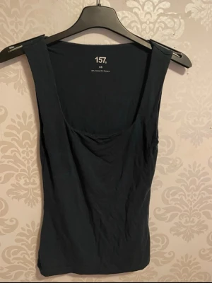 Svart ärmlös linnetopp 157 - En enkel och stilren svart linnetopp från 157. Toppen är ärmlös med rundad halsringning och har en tight passform. Perfekt att matcha med jeans eller kjol för en clean look.