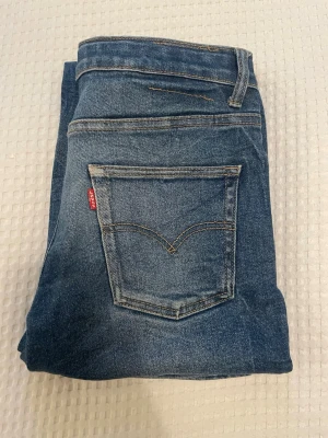 Levis Jeans  - Säljer ett par klassiska blå Levis  jeans med raka ben och snygga slitningar. Jeansen har fem fickor, normal midja och är gjorda i denim. Perfekta för en avslappnad och trendig look. Storleken 14A, 164cm. Hör av dig om du har några frågor eller vill ha några mått!🤩