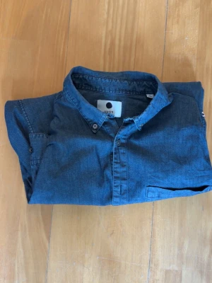 Blå jeansskjorta från NN07 - Säljer en blå jeansskjorta med bröstficka. Skjortan är i bra skick och har inga defekter. Har en slim passform med storleken S. Hör av er vid funderingar.