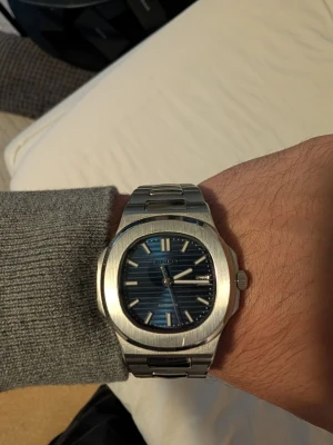 Seiko klocka (Nautilus) - Seiko automatklocka med blå räfflad urtavla, integrerat stållänkarmband och genomskinlig bottenplatta där man ser automatverket.