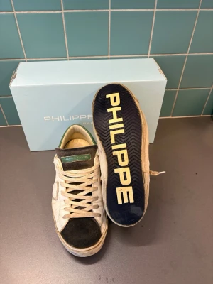 Philippe Model vita sneakers med gröna detaljer - Fräscha och exklusiva läderskor från Philippe Model med gröna detaljer samt svart mocka vid tån. Klassisk låg modell med vita skosnören och PHILIPPE MODEL-tryck under sulan. 