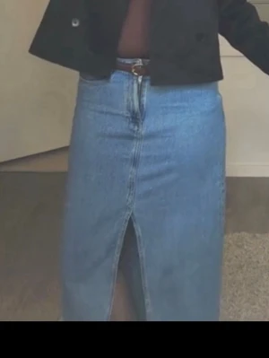 Blå jeanskjol med slits från Zara - Säljer en klassisk blå jeanskjol från Zara med hög midja och slits framtill. Kjolen har en rak passform och är tillverkad i slitstarkt denimtyg. Perfekt att styla med både sneakers och boots.