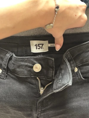 Svarta bootcut jeans från 157 - Säljer ett par svarta bootcut jeans från 157 med klassisk femficksmodell och dragkedja. Jeansen har en snygg, lätt utsvängd passform och silverfärgade knappar. Perfekta till en enkel topp eller hoodie.