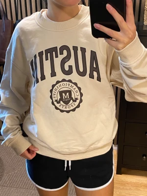 Beige sweatshirt från Divided - Säljer en beige sweatshirt från Divided med trycket 'AUSTIN'. Tröjan har rund halsringning, ribbade muddar vid ärmar och nederkant samt en avslappnad passform. Storlek M, men passar även mig i strlk XS/S