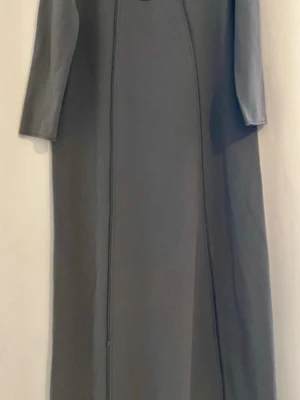 Grå långklänning med trekvartsärm - Stilren grå långklänning med trekvartsärm och minimalistisk design. Klänningen har markerade sömmar framtill och en detalj med knappar på ryggen. Perfekt för dig som gillar enkel och modern stil.