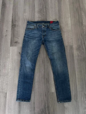 Blå slim fit jeans Hugo - Snygga blå slim fit jeans med lätt slitna detaljer och klassisk femficksdesign. Jeansen har normal midja och raka ben, perfekta till en avslappnad stil. Materialet är denim i bomull med lite stretch för extra komfort.