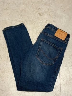 Blå jeans från Jack & Jones - Snygga blå jeans från Jack & Jones med klassisk femficksmodell och bruna kontrastsömmar. Jeansen har en rak passform och är tillverkade i ett mjukt denimtyg. Perfekta för en avslappnad och trendig look.