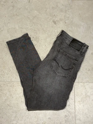 Jack&Jones Jeans - Snygga grå jeans i slim fit-modell med klassisk femficksdesign och svarta sömmar. Jeansen har en diskret tvättad look och är tillverkade i ett mjukt denimtyg som ger en skön känsla. Passar perfekt till en avslappnad stil.