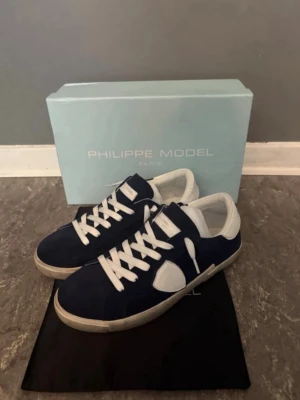 Philippe Model blåa sneakers - Snygga sneakers från Philippe Model i mörkblå mocka med vita detaljer och vita skosnören. Skorna har en klassisk låg siluett och vit sula. Perfekta för dig som gillar stilrena och trendiga sneakers.