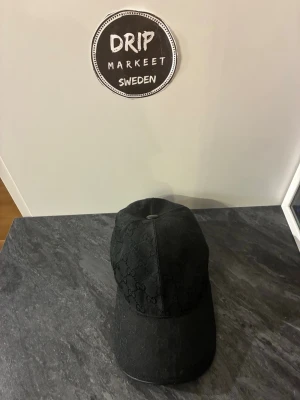 gg svart keps 🧢 - Svart keps med klassiskt GG-mönster och en grön-röd rand på sidan. perfekt för alla för en trendig vardagslook.