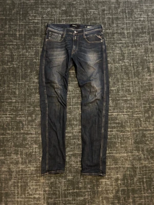 Replay Anbass slim fit jeans - Snygga mörkblå slim fit jeans från Replay med klassisk femficksdesign och kontrastsömmar. Jeansen har en lätt tvättad look med slitningar på låren och bakfickor med dekorativa sömmar. Perfekta för en trendig och avslappnad stil. Jeansen är i storlek W31 och L34