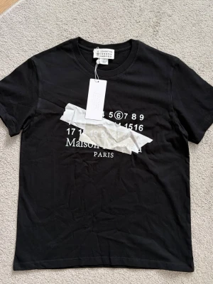 Svart Maison Margiela t-shirt - En svart T-shirt från Maison Margiela, med tryck på framsidan. Storleken är M men sitter som S. Priset går att diskutera.