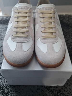 Vita och beige sneakers med gummisula - Snygga sneakers i vitt och beige med ovandel i mocka och läder. Skorna har beige snörning och en klassisk brun gummisula. Perfekt för dig som gillar stilrena och tidlösa sneakers med retrovibbar.