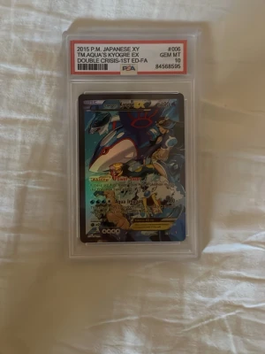 Pokémonkort Kyogre - Obs detta är ett costum gjort Pokémon kort alltså inte orginallt. Japanskt Pokémonkort från 2015, Team Aqua's Kyogre EX Double Crisis 1st Edition. Kortet är graderat av PSA och har fått betyget 10 GEM MT. Kortet har färger i blått, svart och gult och är inneslutet i ett skyddande plastfodral.