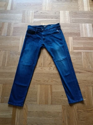 Mörkblå jeans från Replay - Snygga mörkblå jeans från Replay med klassisk femficksmodell och diskret Replay-logga på myntfickan. Jeansen har raka ben och är tillverkade i ett mjukt denimtyg som sitter skönt. Perfekta för dig som gillar stilrena och tidlösa jeans.