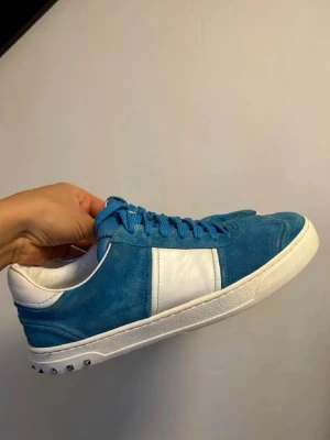 Valentino flycrew i mocka med vita detaljer - Snygga sneakers i blå mocka med vita läderdetaljer på sidan och vit sula. Skorna har blå skosnören och små silverfärgade nitar på hälen. Perfekta för dig som vill ha en unik och stilren look.