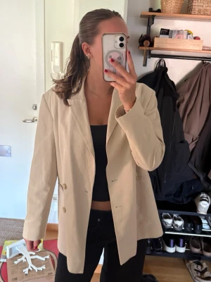 Beige oversized kavaj - Stilren beige kavaj med oversized passform och två knappar framtill. Klassisk krage och raka ärmar. Perfekt att slänga över en topp för en trendig look. Materialet ser ut att vara bomull eller en bomullsblandning.