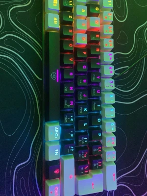 RGB mekaniskt tangentbord 60% - Säljer ett kompakt mekaniskt tangentbord med RGB-belysning. Tangenterna är vita med svarta och färgade tecken, och tangentbordet har en svart ram. Perfekt för gaming eller skrivande, och har en snygg bakgrundsbelysning som kan anpassas.