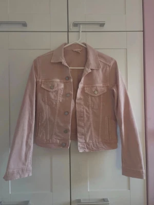 Ljusrosa jeansjacka med fickor - Ljusrosa jeansjacka med knäppning framtill och två bröstfickor samt ”normala fickor”. Jackan är i utmärkt skick. Storlek 36 (s?)