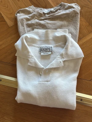 Vit piké henley från CORE  - Säljer en vit piké henley från CORE med klassisk krage och knappar framtill. Skjortan är gjord i bomull och har en enkel, stilren look som passar till många olika outfits. Perfekt för dig som gillar en clean och fräsch stil. Och en vanlig mönstrad T-shirt. 