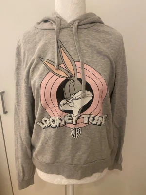 Grå Looney Tunes hoodie med Bugs Bunny - Säljer en grå hoodie med Bugs Bunny och Looney Tunes-loggan i rosa och svart på. Knappt använd. Storlek L (är själv S), så passar också som en oversized-look. 