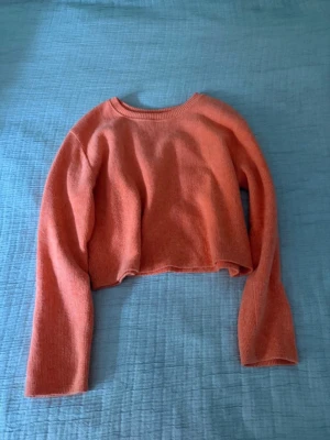Koralröd cropped stickad tröja - Trendig korallfärgad stickad tröja med croppad passform och långa ärmar. Tröjan har rund halsringning och är gjord i mjukt stickat material som passar perfekt till  jeans. Enkel och stilren design utan synligt märke.