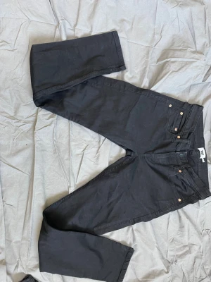 Svarta raka jeans med hög midja - Säljer ett par svarta jeans med rak passform och hög midja. Jeansen har klassiska fem fickor, bälteshällor och knappgylf. Materialet är kraftigt och känns slitstarkt, perfekt till en avslappnad stil.