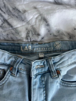 Ljusblå bootcut jeans LAB Industries - Säljer ett par ljusblå jeans från LAB Industries i storlek 152. Jeansen har klassisk femficksmodell, utsvängda ben och bälteshällor. Perfekta för dig som gillar retrovibbar och relaxed stil. Materialet är mjukt denimtyg i bomull.