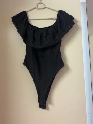 Svart off shoulder body med volang - Säljer en svart body med off shoulder-modell och bred volang runt axlarna. Bodyn har en håldetalj som ger en snygg look. (Vikt in den känsliga delen för att ge en starkare vision). Ny utan prislapp, aldrig använt. Se bion🫶🏻