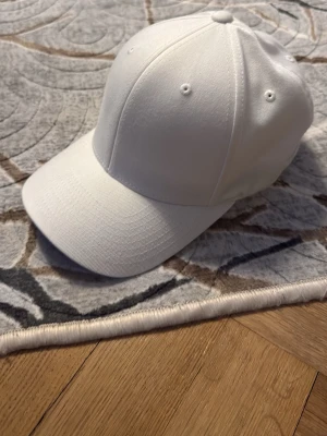 Vit klassisk keps Flexfit XS-S - Snygg vit keps från Flexfit i storlek XS-S. Kepsen har en böjd skärm, sex paneler och små ventilationshål för extra komfort. Tillverkad i ett mjukt och flexibelt material som sitter skönt på huvudet. Perfekt för en clean och stilren look.