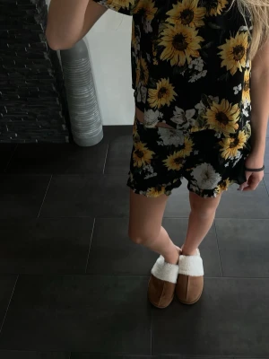 Svart pyjamasset med solrosor - Säljer ett svart pyjamasset med stora gula solrosor och vita blommor. Setet består av en kortärmad topp och matchande shorts, båda i mjukt och lätt material. Perfekt för mysiga kvällar hemma.