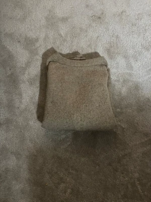 Beige stickad tröja med rund hals - En enkel och stilren beige stickad tröja med rund hals och långa ärmar. Tröjan har ribbstickade muddar vid ärmslut och nederkant. Perfekt för lager på lager och passar till det mesta i garderoben.