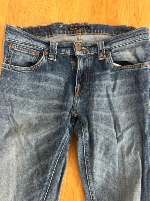 Blå jeans från Nudie Jeans Co - Säljer ett par klassiska blå jeans från Nudie Jeans Co i storlek W28 L32. Jeansen har en snygg tvätt med slitningar och kontrastsömmar. Femficksmodell med normal midja och raka ben. Perfekta till en avslappnad stil.