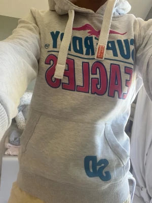 Superdry hoodie - Grå hoodie med blått och rosa tryck. Snygg passform. Storlek S, men passar även xs då den är lite mer åtsittande💕
