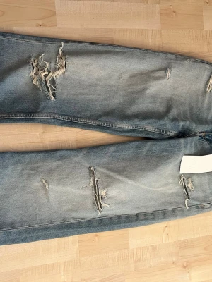 Wide leg jeans från ZARA, ljusblå - Säljer ett par trendiga wide leg jeans från ZARA i ljusblå tvätt. Jeansen har slitna detaljer och hål på benen för en avslappnad och cool look. Perfekta för dig som gillar en loose fit och vill ha en modern streetstyle. Helt nya prislapp kvar!! Ut gångs pris 520!!